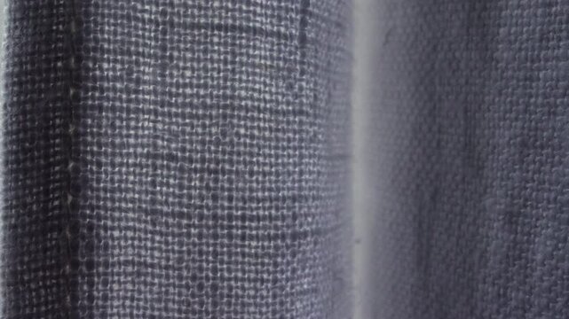 Close up of gray fabric curtain texture near window, soft interior detail with natural light and woven material pattern