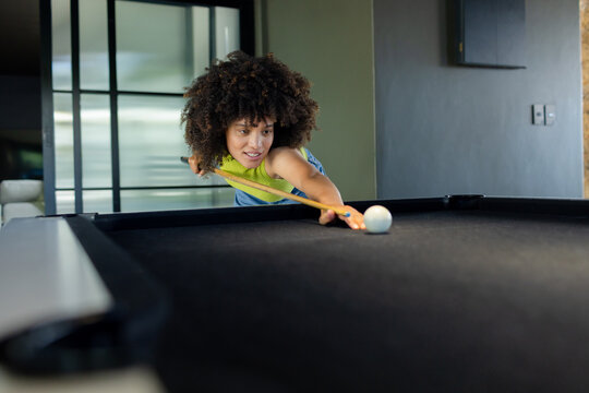 Woman wearing lime-green top aiming cue ball on black pool table in home using bridge hand