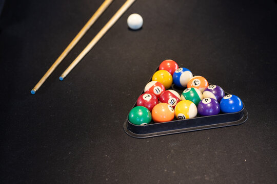 Triangular rack holding 15 glossy numbered balls on dark felt, cues lying diagonally, copy space