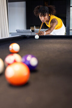 African American woman lining up cue on black-felt pool table in game room wearing yellow top