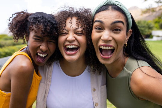 African American friends laughing together outdoors in park, wearing yellow white olive tops
