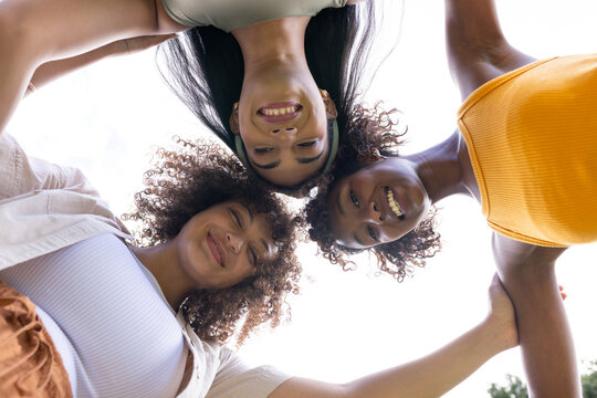 African American women leaning smiling linking shoulders around low camera in park in tank tops