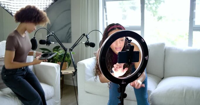 Female co-hosts adjusting ring light, phone mount and boom mics in living room preparing podcast