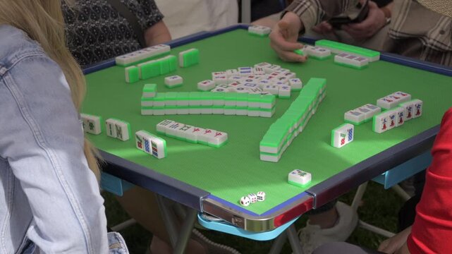This video shows a close up view of people gathered around a table playing mahjong.