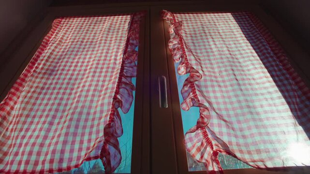 Red and white checkered curtains covering chalet window, sunlight glowing through gingham fabric inside rustic alpine home