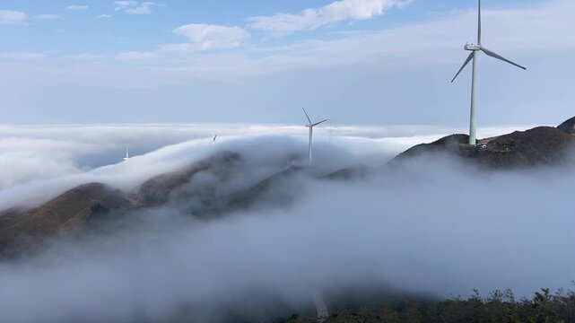 A spectacular time-lapse shot capturing rotating wind turbines amidst a rolling sea of clouds on a mountain ridge at dawn in Laiyuan, Hebei, China.