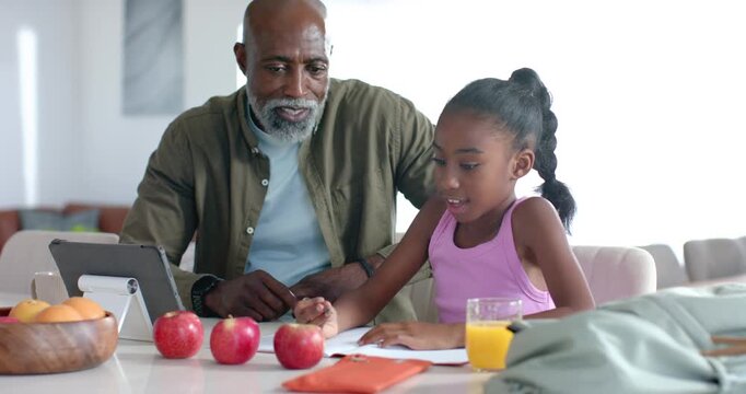 African American senior man guiding school child, pointing tablet, 3 apples while teaching counting
