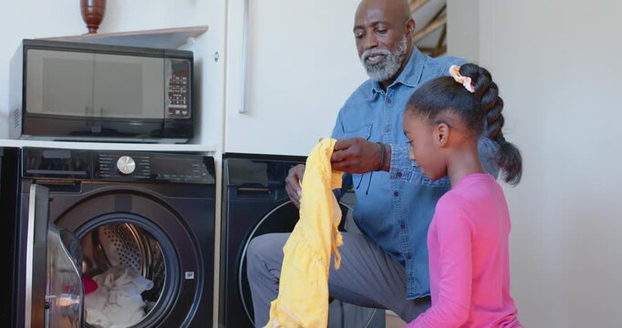 African man opening washer, unfolding yellow dress with girl watching at home, checking for stains