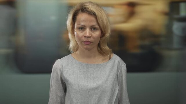 Young blonde woman standing and giving thumbs up gesture in teal building; confidence determination.
