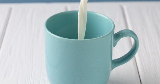 Pouring fresh milk into mug at white wooden table, closeup
