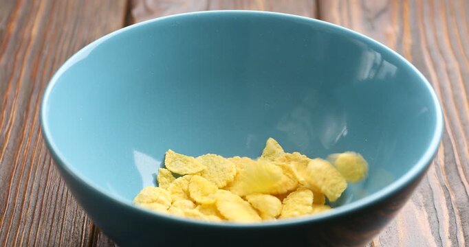 Dropping corn flakes into bowl at wooden table, closeup