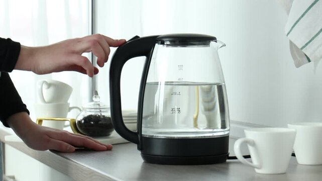 Woman turning on electric kettle indoors, closeup