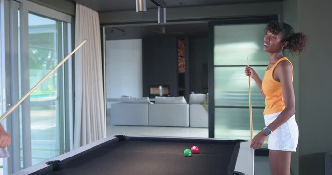 African American female friends playing pool at home for fun, initial cue striking scattering balls