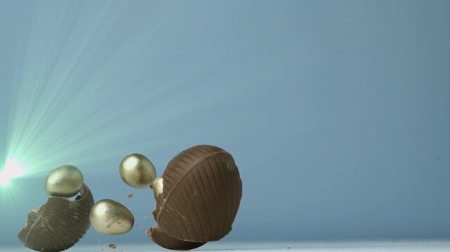Dropping milk-chocolate egg rotating and splitting from above, revealing three metallic-gold eggs