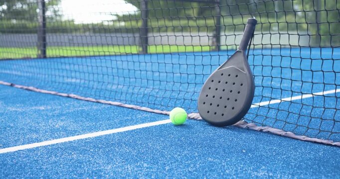 Camera panning right, zooming in to frame black padel racket and neon ball at net line