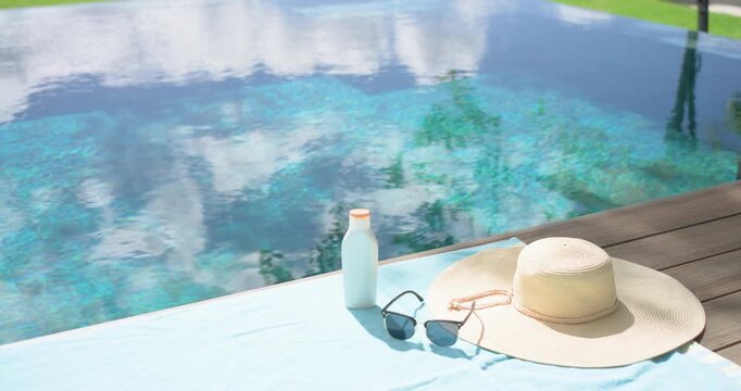 Camera is pulling back, tilting up to reveal light-blue towel, hat, sunglasses, bottle on pool