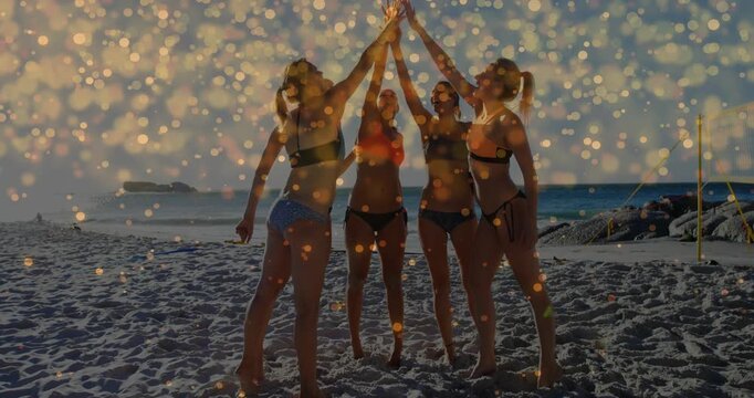 Forming circle, 4 women joining hands overhead on beach cheering, bokeh overlay on hands for travel