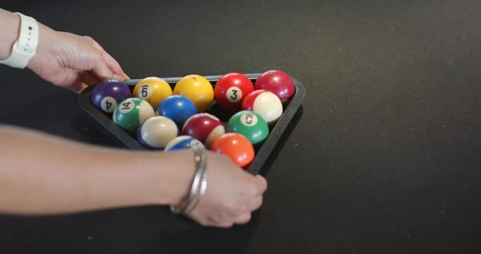 Adult female hands entering sides, arranging pool balls into triangle rack on pool table for break