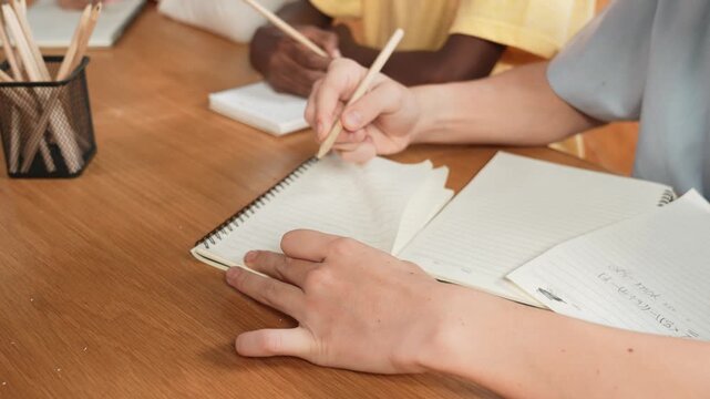 Close up of young diverse boy hand write answer down in a paper. Cropped of smart multicultural high school student taking a note or drafting idea at book. Creative education concept. Edification