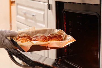 Female baker's hand taking baking tray with tasty croissants from oven in kitchen