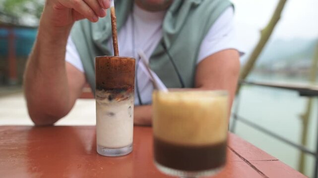 Outdoor Cafe Coffee Ritual. Closeup Of Hand Blending Iced Coffee. Detailed View Of Coffee Being Stirred Outdoors. Intimate Coffee Tasting Moment Captured At Outdoor Cafe Setting