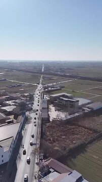 Baoding, Hebei/China - March 4, 2026: A vertical drone shot flying forward over a busy road with car traffic passing through the outskirts of a town in Hebei.