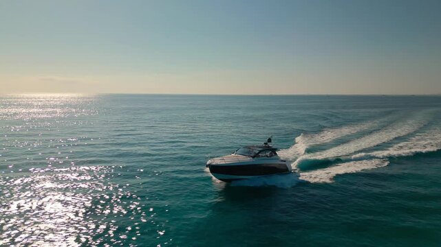 Aerial drone view of a luxury boat cruising across a calm ocean in Miami, Florida with sunlight reflecting on the sea.