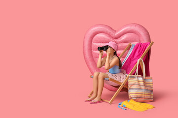 Cute girl with binoculars and inflatable mattress sitting in deck chair on pink background © Pixel-Shot