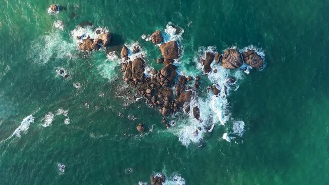 4K top-down aerial view of ocean waves crashing against rugged rocks in vibrant turquoise water