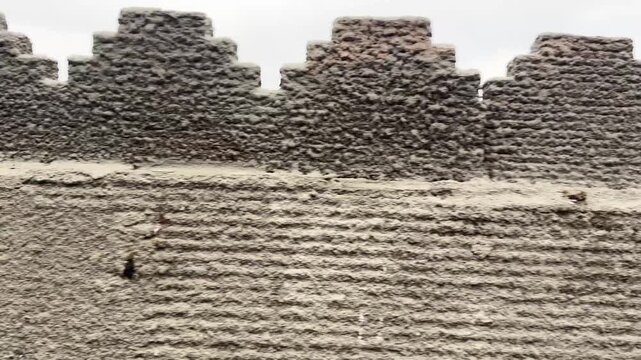 Old battlement of an ancient castle city wall in China, showing weathered stone crenellations with a blurred pathway and cloudy sky in the background, highlighting historical architecture and defensiv