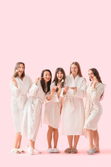 Fototapeta premium Group of young women in bathrobes doing makeup on pink background. Hen Party