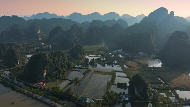 Aerial view of rice paddies and limestone mountains in Ninh Binh, Vietnam. Farmers cultivate rice, a staple crop, in the flooded fields of the countryside.