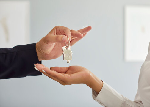 Professional realtor giving buyer key to new home. Close up cropped shot of male real estate agent hand handing keys from new apartment to young female customer. Concept of property purchase or rent.