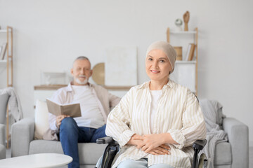 Fototapeta premium Mature woman after chemotherapy in wheelchair and her husband reading book at home