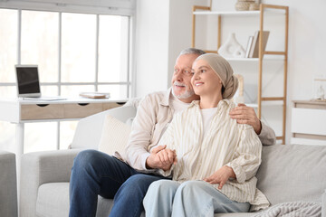 Mature woman after chemotherapy with her husband hugging on sofa at home