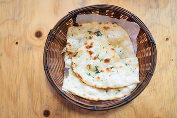 Top view of freshly baked garlic naan bread served in a wicker basket on a wooden table