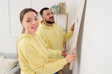 Fototapeta premium Young couple hanging painting on light wall at home