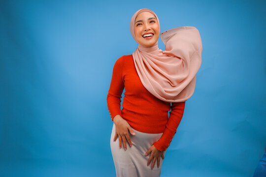 Gorgeous young Asian Muslim woman with hijab waving in the wind, modelling pose on blue background.