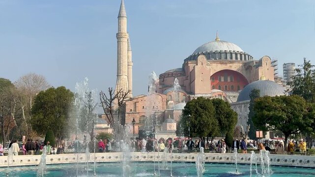 Stunning view of Hagia Sophia Grand Mosque with a splashing fountain in the foreground. Iconic Istanbul landmark under a blue sky. Historic Byzantine and Ottoman architecture.