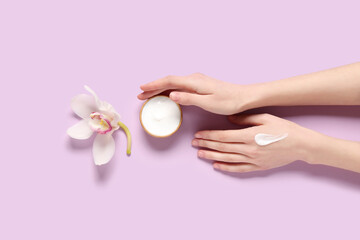 Beautiful female hands with jar of cosmetic cream and orchid flower on lilac background