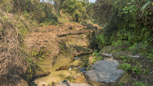 A winding stream flows through a gorge among the rocks. Green plants on cliffs. Nepal. Pokhara. Davis Falls.  Paatal Ko Chango. Underworld&rsquo;s Waterfall