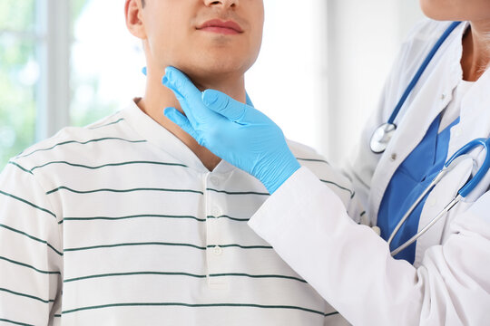 Female endocrinologist examining thyroid gland of man in clinic
