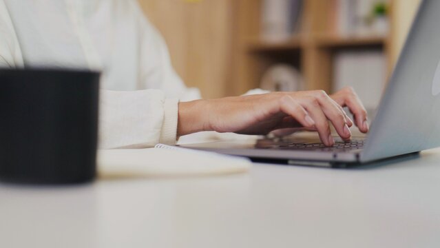 Close-up of Asian woman's hands typing on laptop keyboard