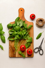 Wooden board with fresh green basil and tomatoes on white background