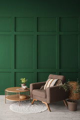 Naklejka premium Cozy armchair, coffee table and houseplants near green wall