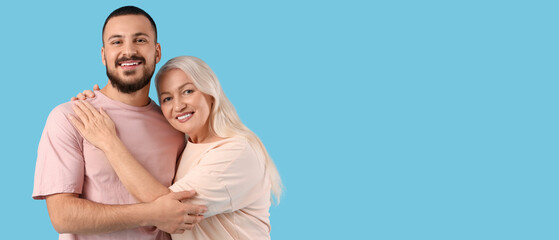 Fototapeta premium Young man hugging his mother on blue background
