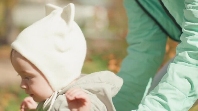 Caucasian toddler exploring park on own, soft bonnet and hooded coat, tentative steps through fallen leaves with parent nearby, curious profile closeups, sunlight filtering through trees, childhood