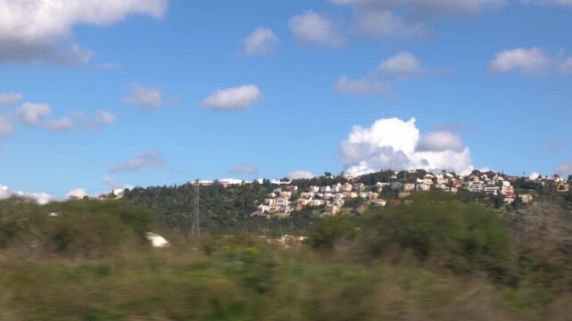 A view from a train window of a city: towns and houses under a cloudy sky during the day. Traveling through Israel by train. Train between Haifa and Tel Aviv. Travel and adventure in Israel.