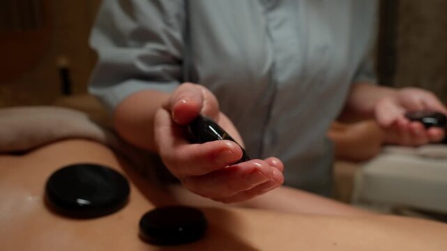 Relaxing hot stone therapy session with therapist placing warm polished stones on oiled back to relieve muscle tension and promote deep body relaxation