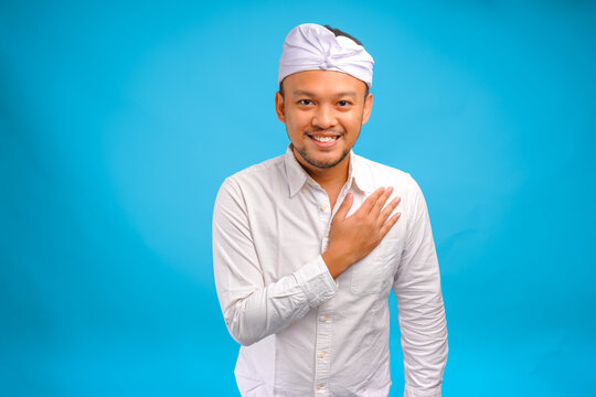 Cheerful young Balinese man wearing traditional udeng doing greeting or respecting gesture.